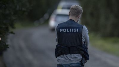 En polis med ryggen mot kameran står på en grusväg. Polisen har en väst på sig. Det står "poliisi" på ryggen.