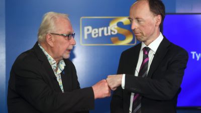 Matti Putkonen och Jussi Halla-aho gör en så kallad "fistbump" framför en blå Sannfinländar-plansch.