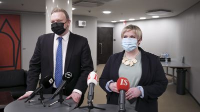 Antti Kurvinen och Annika Saarikko i munskydd står vid ett podium med många mikrofoner.