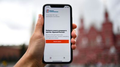 En hand håller upp en telefon, med en text på ryska som lyder: "Hitta din kandidat mot Enade Ryssland".