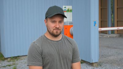 Ung man i keps och grå t-skjorta står framför en blå port.