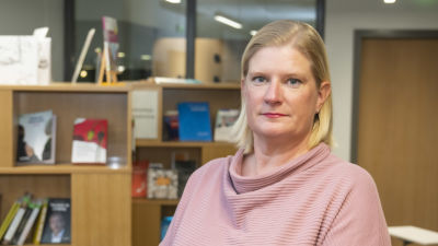 En kvinna i rosa tröja står framför en bokhylla.