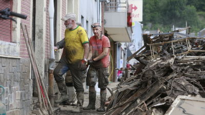 Två volontärer deltar i röjningsarbeten utanför ett ödelagt hus.