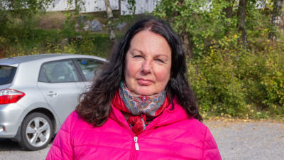 En medelålders kvinna med mörkt år och pink jacka tittar in i kameran.