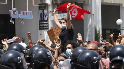Kvinna med munskydd och Tunisiens flagga i händerna.
