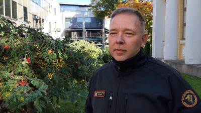 Niklas Guseff, en man med grånande hår och en Gränsbevakaruniform, står på en gård med höstgula träd.
