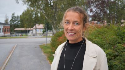 Blond kvinna i vit jacka står på en trottoar.