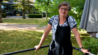 En kvinna som står och håller i ett räcke framför en park.