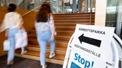 Etualalla kyltti, jossa lukee "äänestyspaikka" ja on nuoli. Takana kaksi naista kävelee nuolen osoittamaan suuntaan.