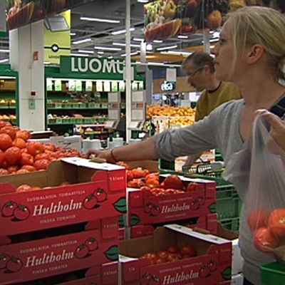 Nainen poimii kaupassa tomaatteja pussiinsa.