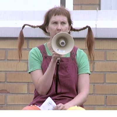Kirjastonhoitaja Arja Palonen pukeutuneena Peppi Pitkätossuksi. Kädessään megafoni.