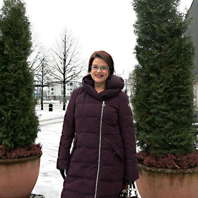 Nainen seisoo ulkona havupuiden vieressä.