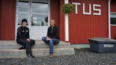 Två kvinnor sitter på trappan till en röd träbyggnad.