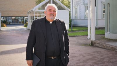 Man i svart kostym och prästkrage står på en innergård.