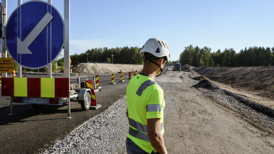 Man i arbetskläder och skyddshjälm står vid vägbygge.