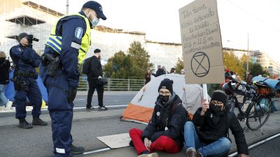 En polis står och talar med två Elokapina-demonstranter som sitter på gatan.