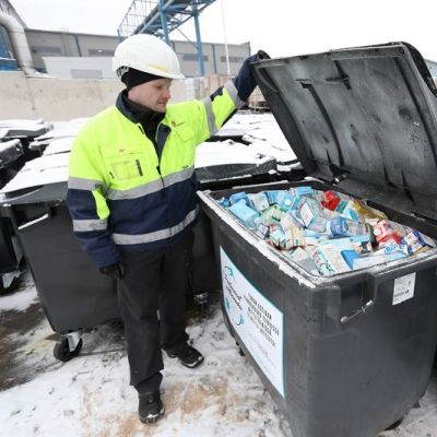 Mies pitää jäteastain kantta ylhäällä. Astiassa maitopurkkeja.