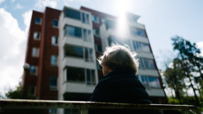 Kvinnlig pensionär på bänk utanför ett höghus.