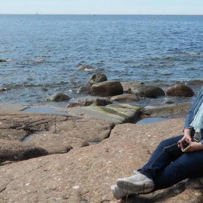 Merja Naroma istuu rantakalliolla Kirkonmaan eteläkärjessä taustanaan Itäinen Suomenlahti.