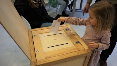 En liten flicka lägger en röstsedel i en valurna.