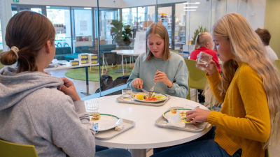 Tre flickor sitter vid ett runtbord i Vårberga skolas matsal och äter skollunch.