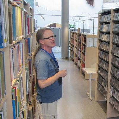 Reijo Holm tarkastelee Kokkolan kirjaston musiikkiosastolla hyllyjän välissä. 
