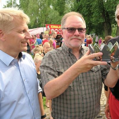 Kolme miestä lähikuvassa Elomessut taustanaan