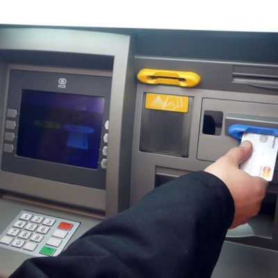 Käsi laittaa luottokorttia pankkiautomaatin siniseen kortinlukijaan.