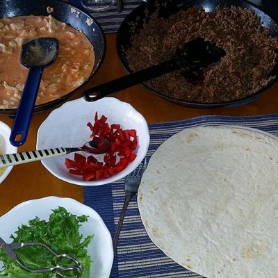 Kuvassa tortilla-aineksia kupeissa ananaspaloja, pannussa broileria, vihanneksia ja tortillapohjia.