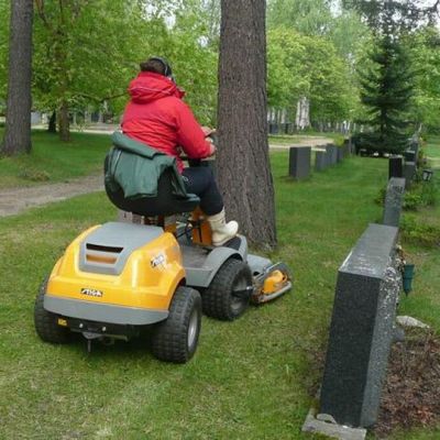 Kesätyöntekijä ajaa ruohoa hautausmaalla.