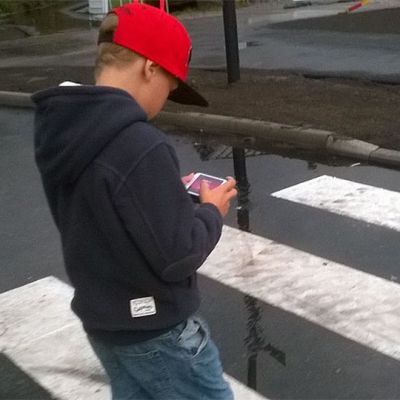 Lapsi tuijottaa kännykkäänsä suojatiellä