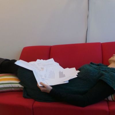 nainen makaa sohvalla paperipino sylissään