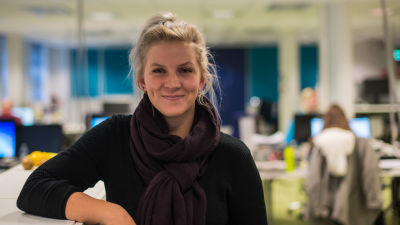 Jenni Ahlbäck står lutad mot ett dokumentskåp, i bakgrunden ett kontorslandskap.