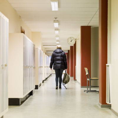 En ensam flicka med ryggen vänd mot kameran går i skolkorridor