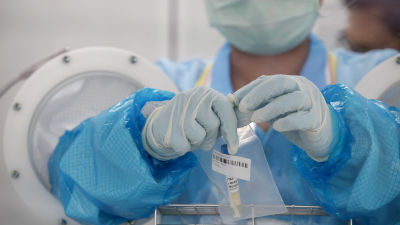 En person i skyddsutrustning håller i ett coronavirus-provsvar.