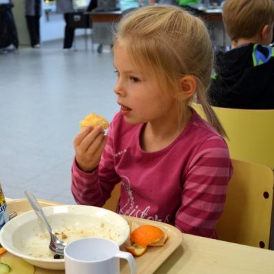 Neela Hukkanen syö appelsiinia Siilinjärven Toivalan koulun ruokalassa. Tarjottimella on jäätelötuutti.