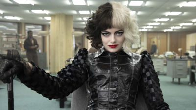 Närbild på Cruella (Emma Stone) som sitter och ser klurisk ut.
