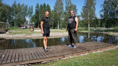Två män står vid en damm. I bakgrunden syns en lekpark.
