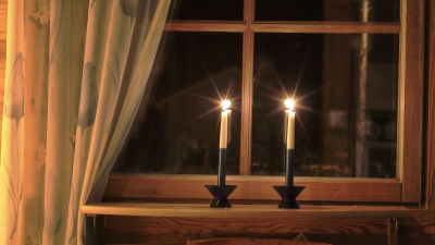 Två blåvita ljus brinner i ett fönster på kvällen.