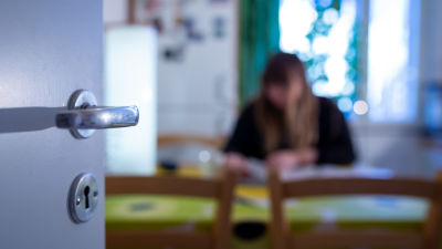 En anonym kvinna sitter i ett kök. Bilden är suddig så att man inte kan urskilja vem hon är.