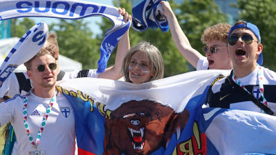 Tre finska fotbollsfans med halsdukar med texten Suomi. I mitten ses ett ryskt fotbollsfan med en rysk flagga i handen.