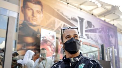 Lewis Hamilton står framför en vägg med Max Verstappens ansikte på.