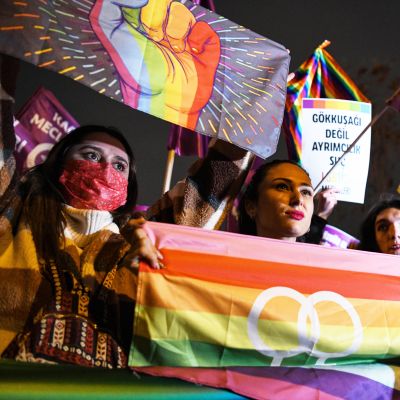 Mielenosoitukseen osallistuvat naiset kannattelevat sateenkaarilippua ja väkivallan vastaisia symboleja sisältäviä banderolleja mielenosoituksessa Turkissa.