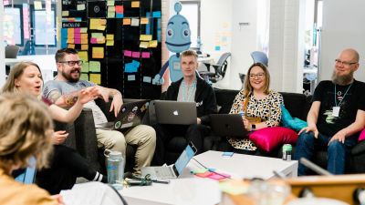People sitting in two sofas in front of a kanban board.