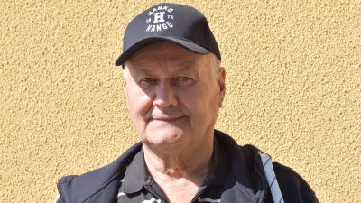 En man med keps som det står Hangö-Hanko på ser in i kameran. Utomhus