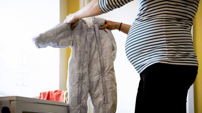 Gravid kvinna håller i en babyoverall.