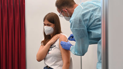 En ung kvinna får en vaccinspruta och lyfter upp t-skjortsärmen