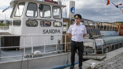 Albert Lass står i kaptenshatt och vit skjorta framför skeppet Sandra D.