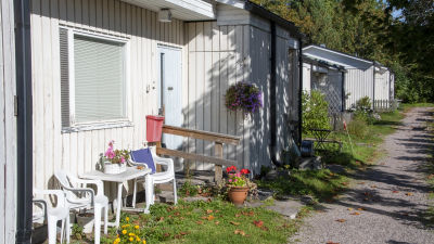 Ett vitt radhus i ett plan. Plaststolar och blomkrukor längs väggen.