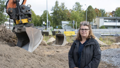 Catarina Helenius står framför en grävskopa som är beredd att börja bygga de nya bostäderna i hörnet av Alexandersgatan och Sibeliusbulevarden i Borgå.
